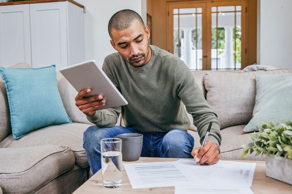 Man filling out paperwork while using his digital tablet.