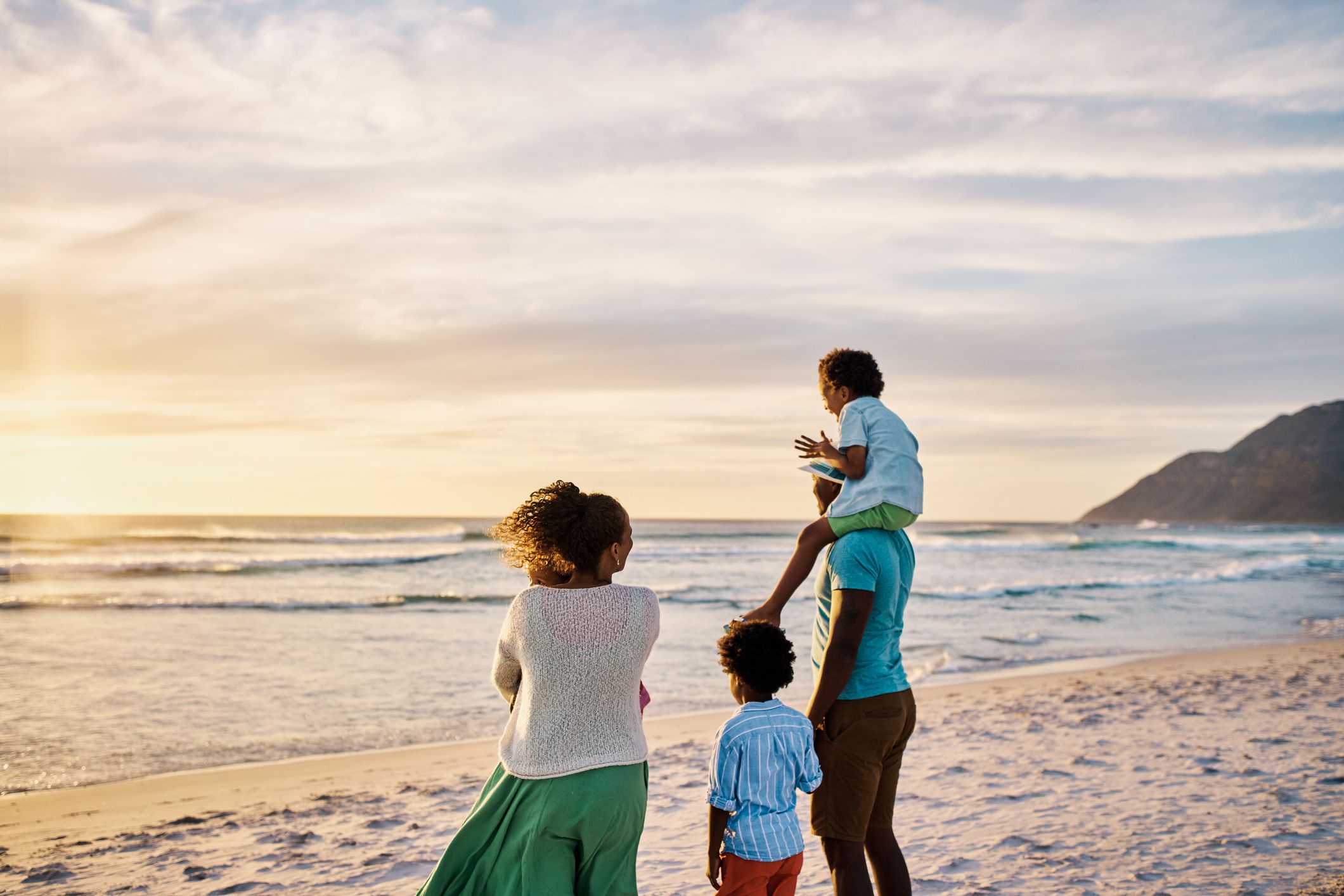 A family on the beach admiring the scenic sunset view and calm waves from behind during a fun summer vacation together
