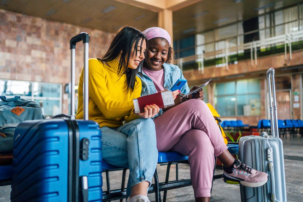 Young cheerful multi racial women friends looking at travel insurance prices at the airport while waiting for their flight