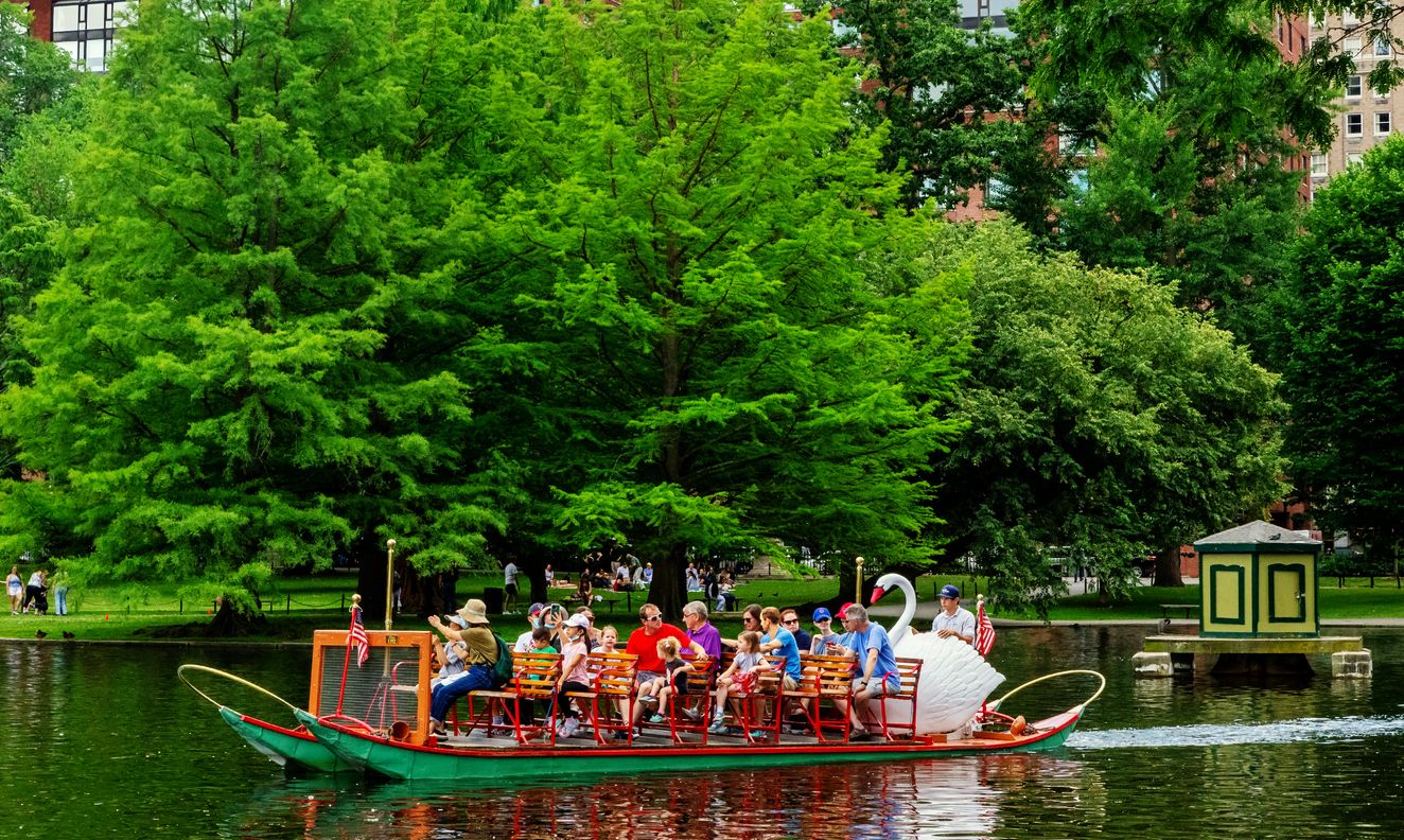 Swan boat full of people traveling across the Boston Public Garden pond