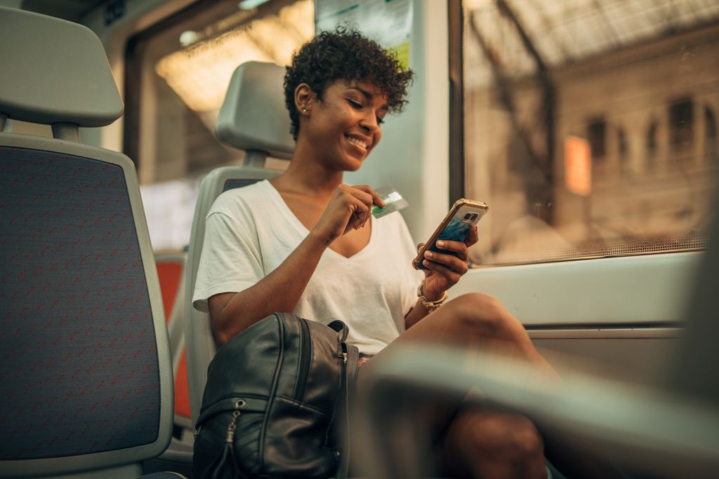 Woman in train using phone and credit card for shopping online