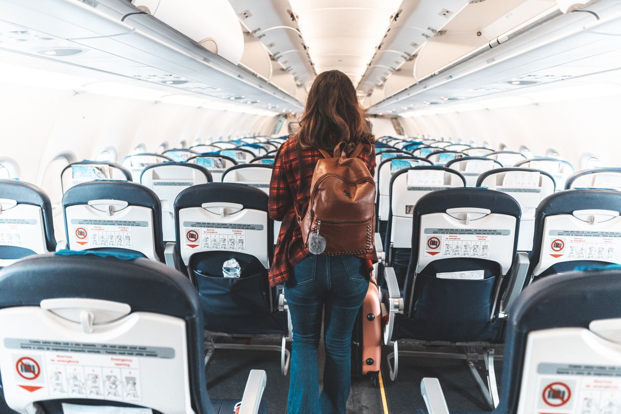 Airplane interior with empty seats and a woman boarding.