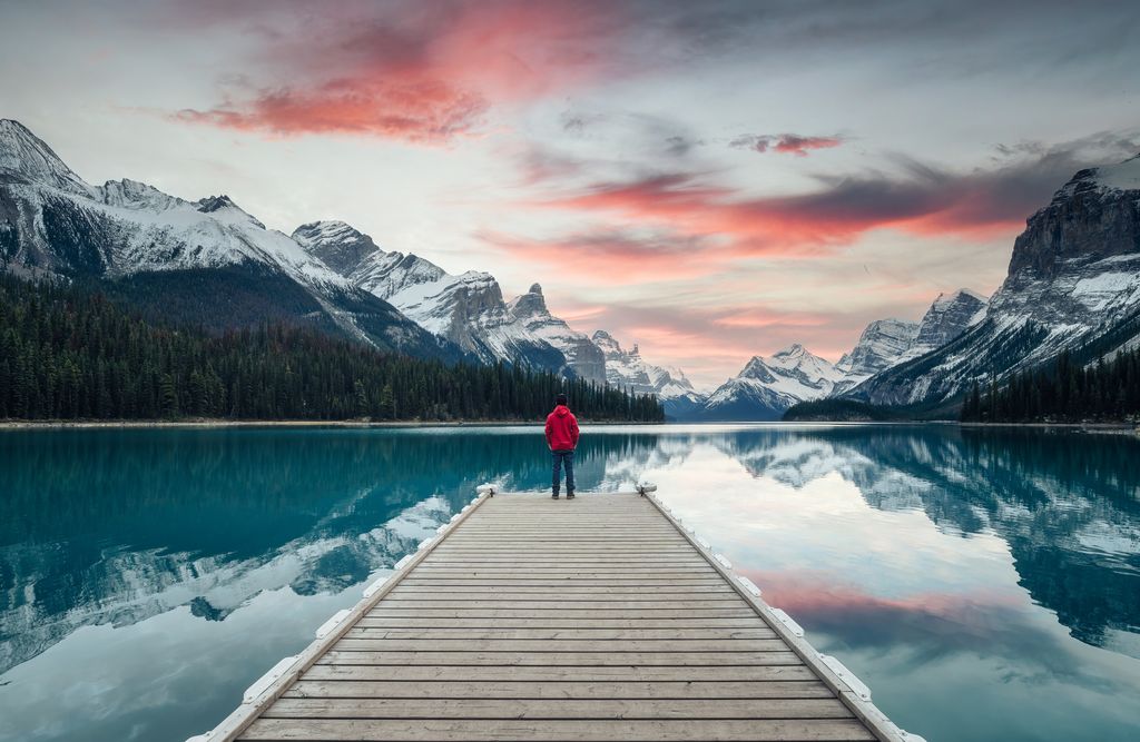 Spirit Island with male traveler enjoying on pier at the sunset in Maligne Lake, Jasper National Park