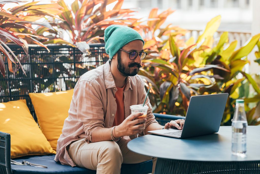 Young man smiling while working on his laptop at a coffee shop
