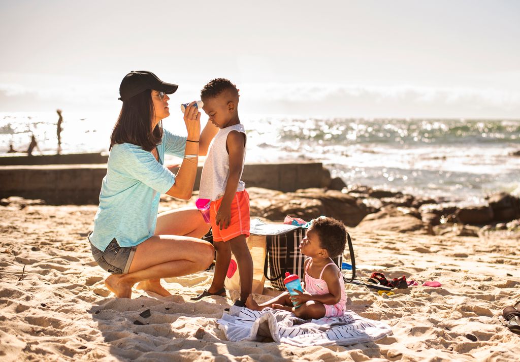 Mom putting sunscreen lotion on her little children at the beach