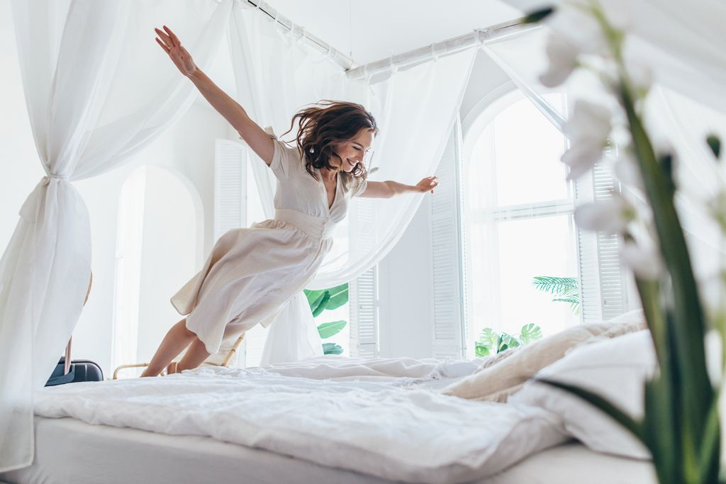 Woman jumps on white hotel bed