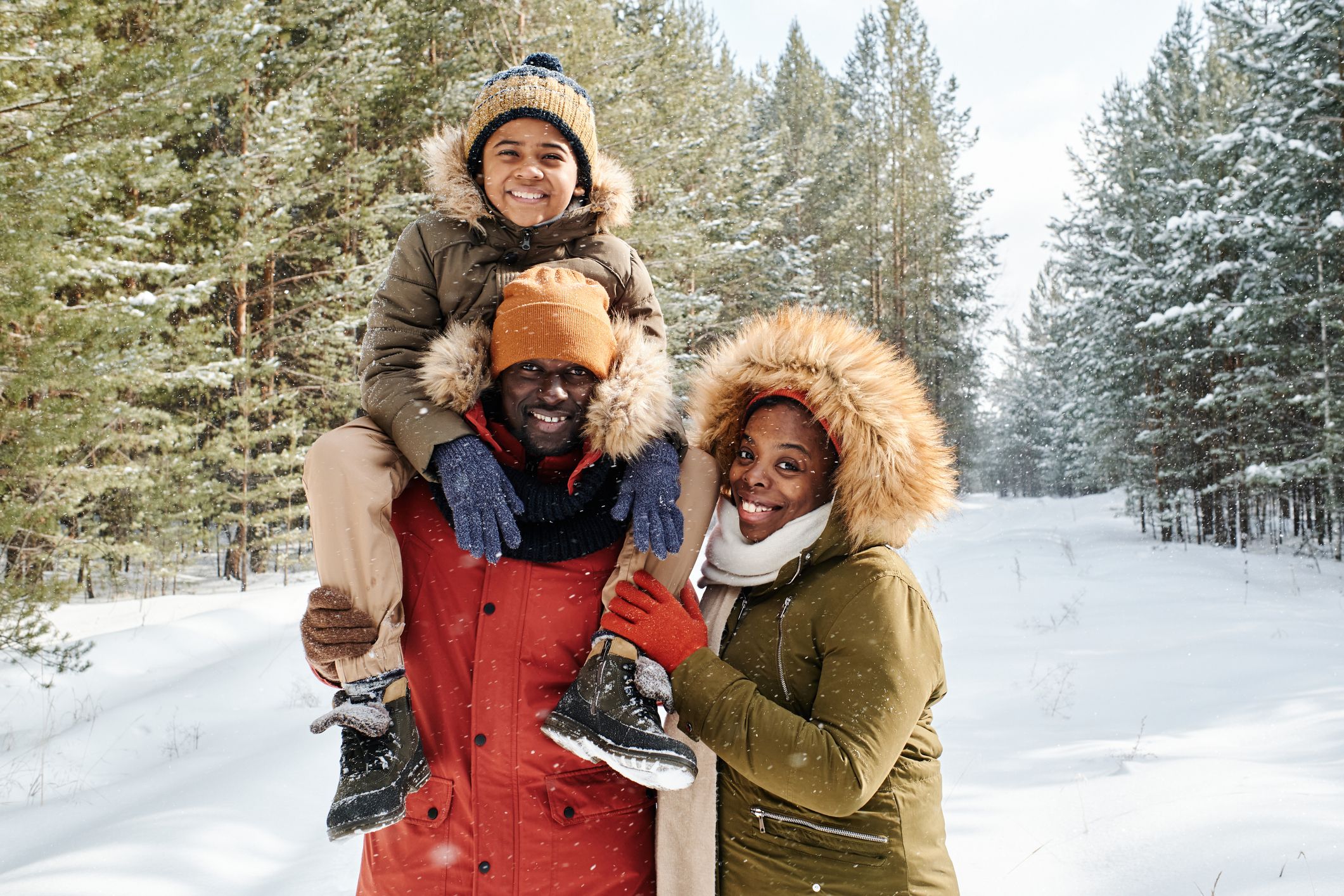 Cheerful family of three in warm winterwear spending day in winter forest