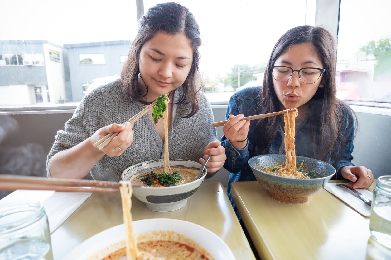 Personal perspective of Eurasian millennial sisters eating steaming vegan ramen with kale. Vancouver, British Columbia, Canada.