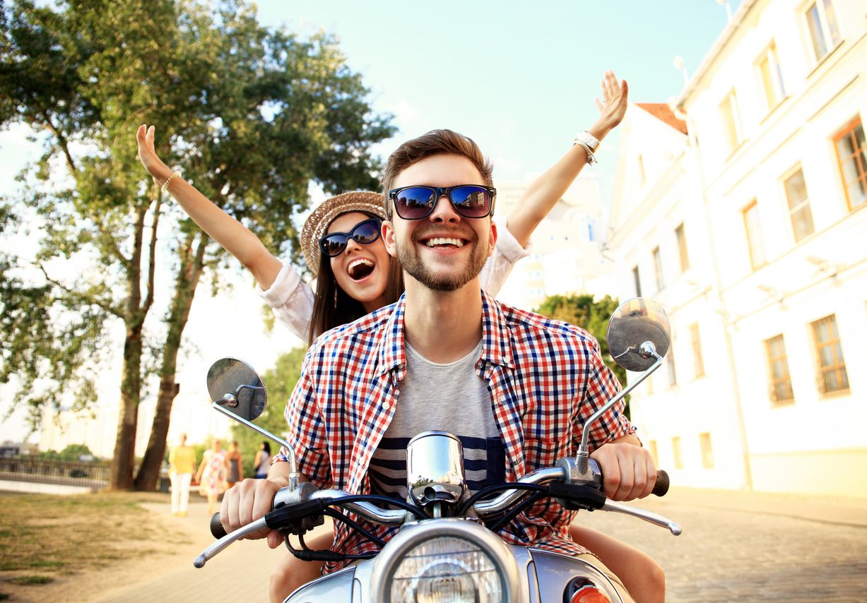 Portrait of happy young couple on scooter enjoying road trip.