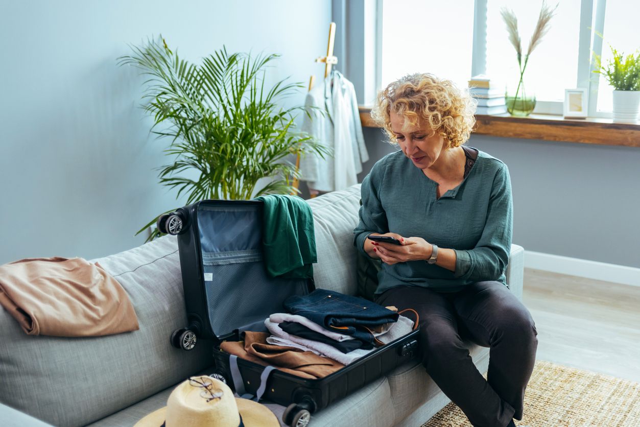 Woman using mobile phone while packing her bags for travel.