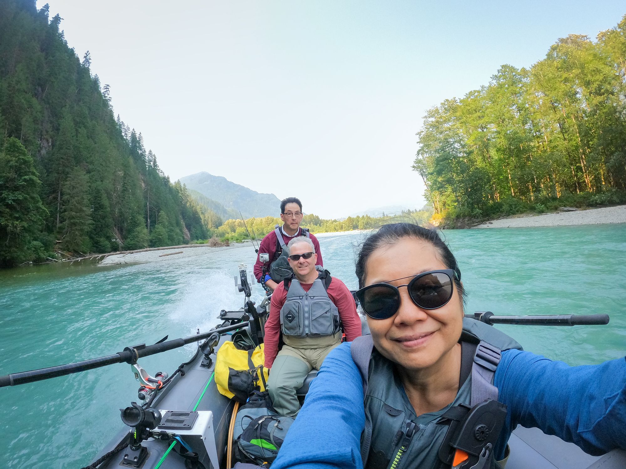Senior woman taking selfie of friends traveling on an inflatable boat in remote glacier fed turquoise colored river to go freshwater fishing.