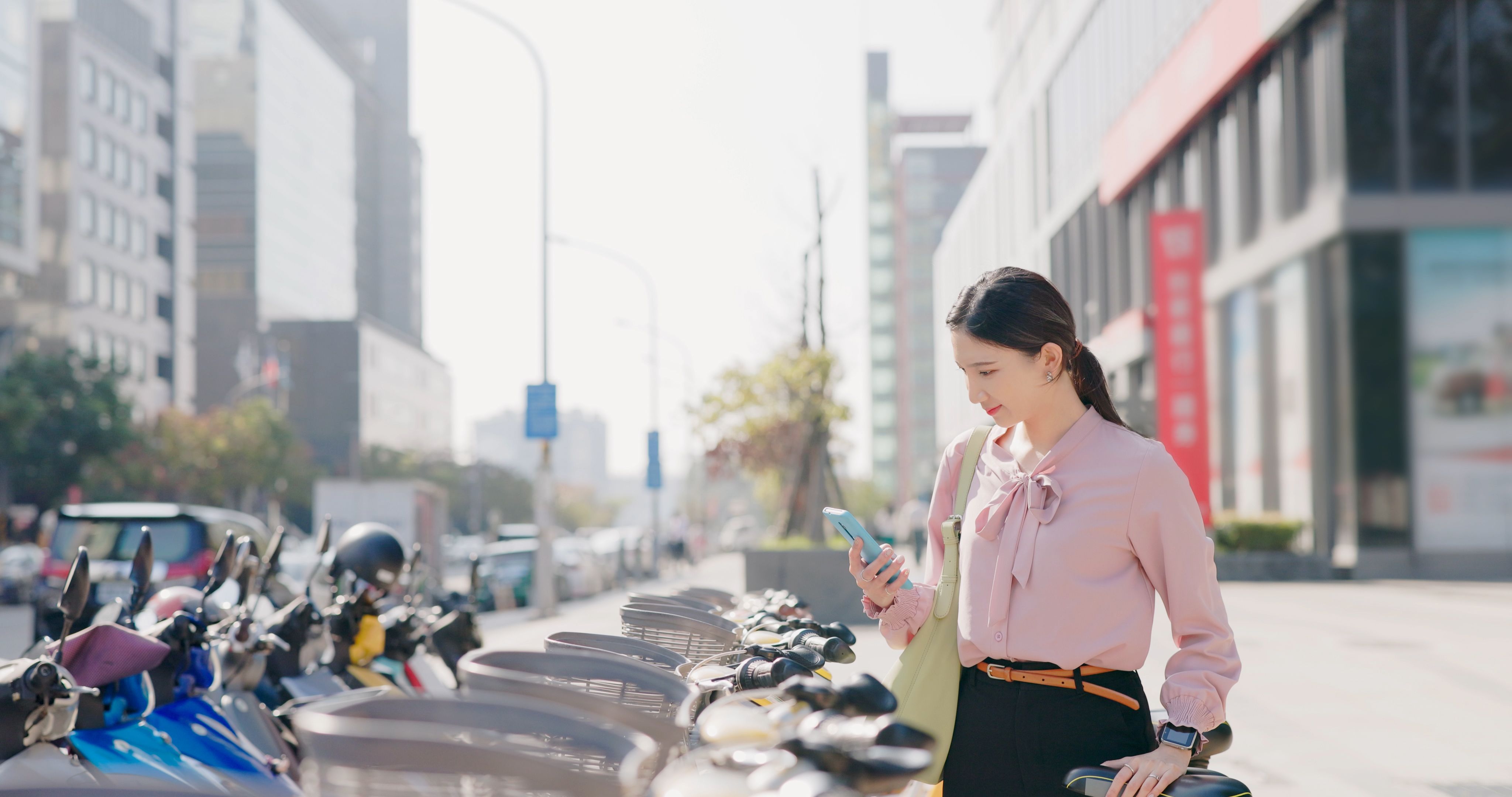 Businesswoman using phone to rent and ride a bike commuting in the city