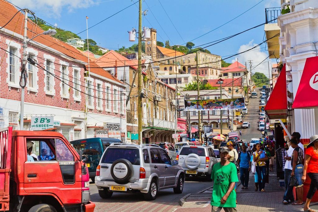 scene of daily life in the capital of Grenada, with people walking on the sidewalks and traffic in the streets