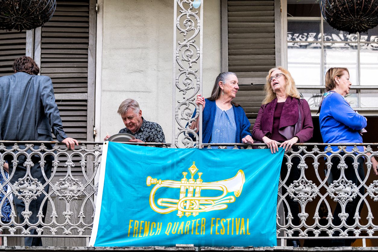 Old town street in New Orleans with people on balcony by French Quarter Festival sign