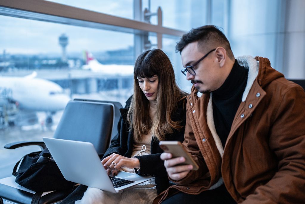Young couple using the laptop and the mobile phone in the airport.