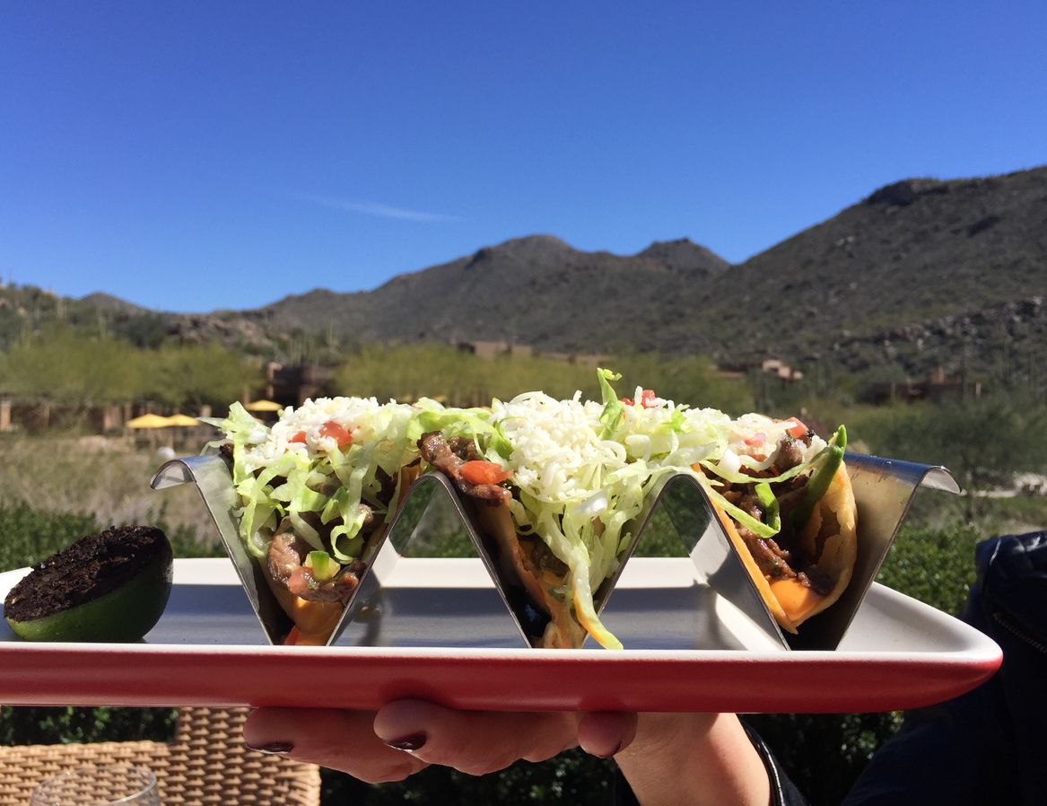 A woman’s hand holds a trio of buffalo tacos overlooking the foothills of the Sonoran Desert in Tucson, Arizona