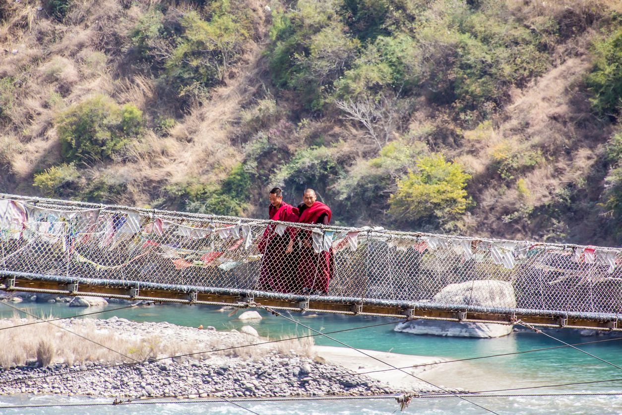 Two monks are walking over Bhutans longest suspension bridge near the dzong of Punakha, Bhutan