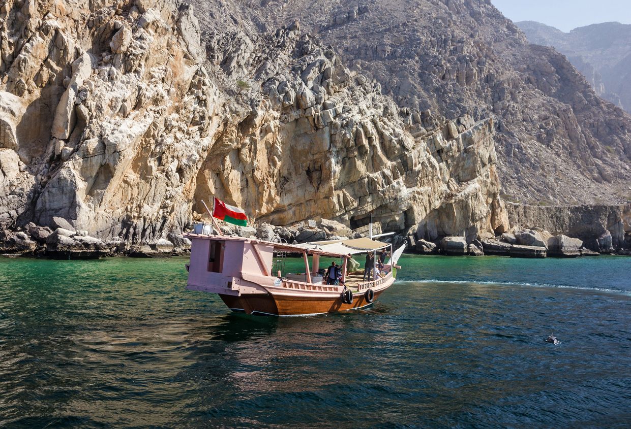Khasab, Oman: Dolphins and tourist dhow boats, fjords of Musandam peninsula
