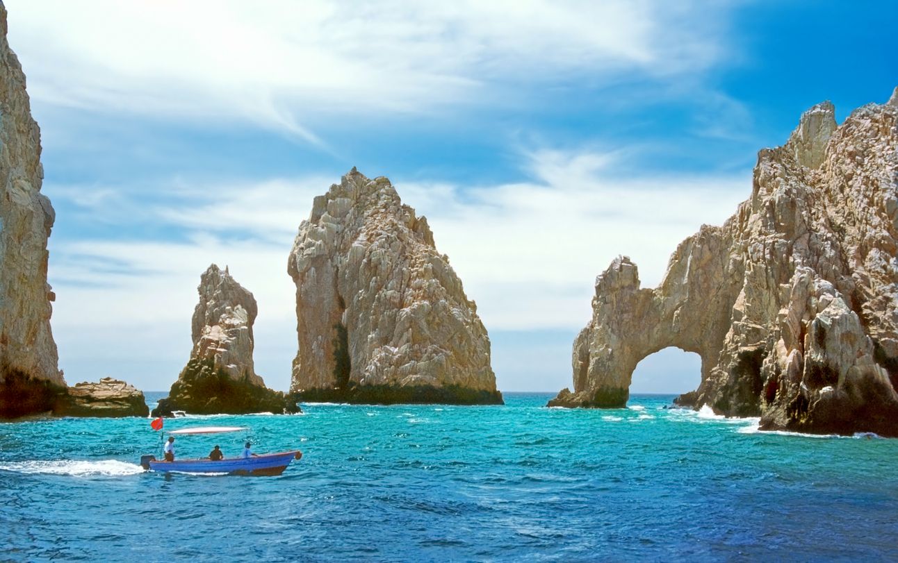 Inside the bay at Cabo San Lucas, a small tourboat is dwarfed by rock formations including the famous El Arco.