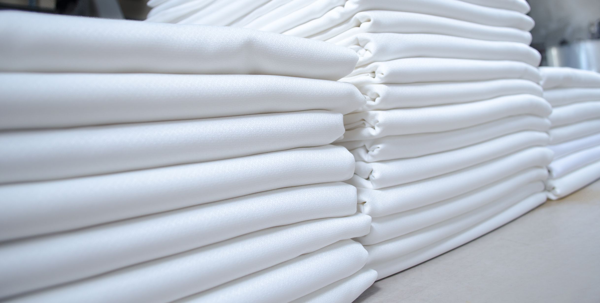 Stacks of folded white fabrics or sheets in a laundry