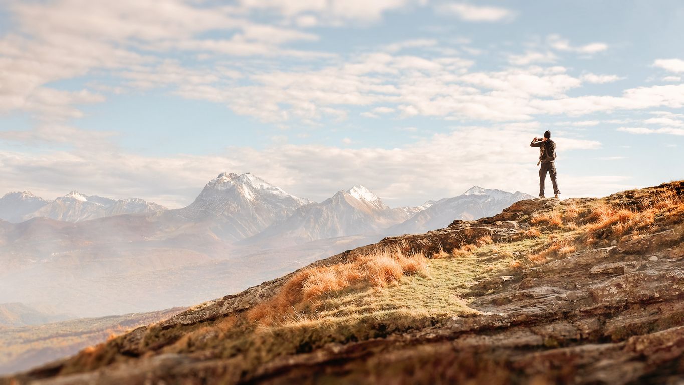 Male traveler on top of a rock taking pictures of majestic mountain landscape.