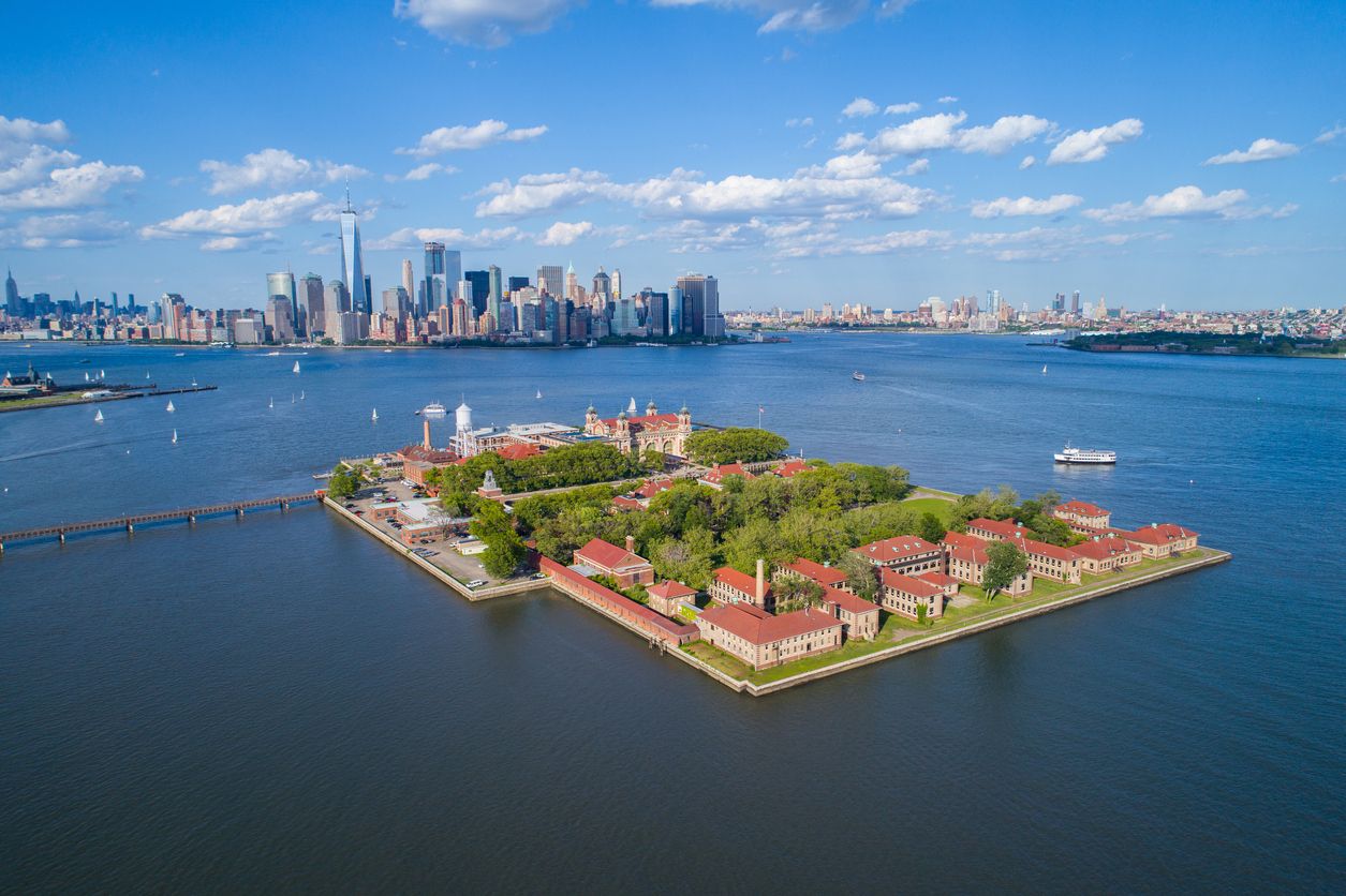 Aerial view of Ellis Island with a tour boat and Lower Manhattan Skyline in the background.