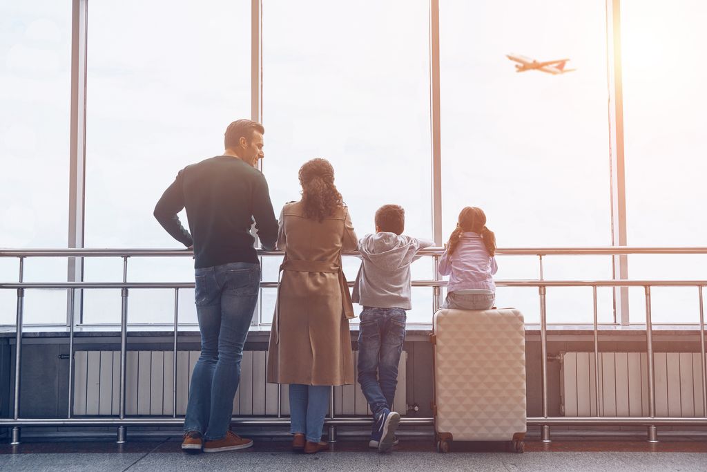 family with two little kids looking at the flying airplane while standing in airport terminal
