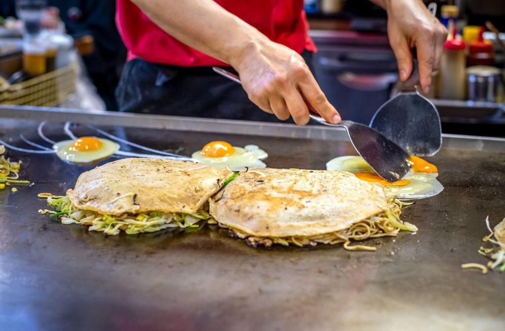 chef is cooking Okonomiyaki with fried eggs on the iron plate typical from Osaka and Hiroshima