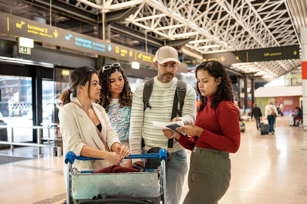 Group of young travelers using smartphone checking flight or online check-in at airport together, with luggage