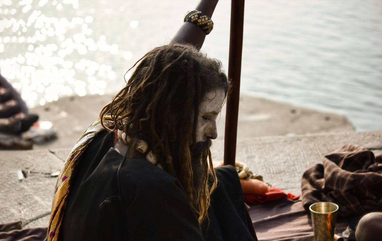 Aghori baba with closed eyes sitting with a stick against ganges river in Varanasi, India