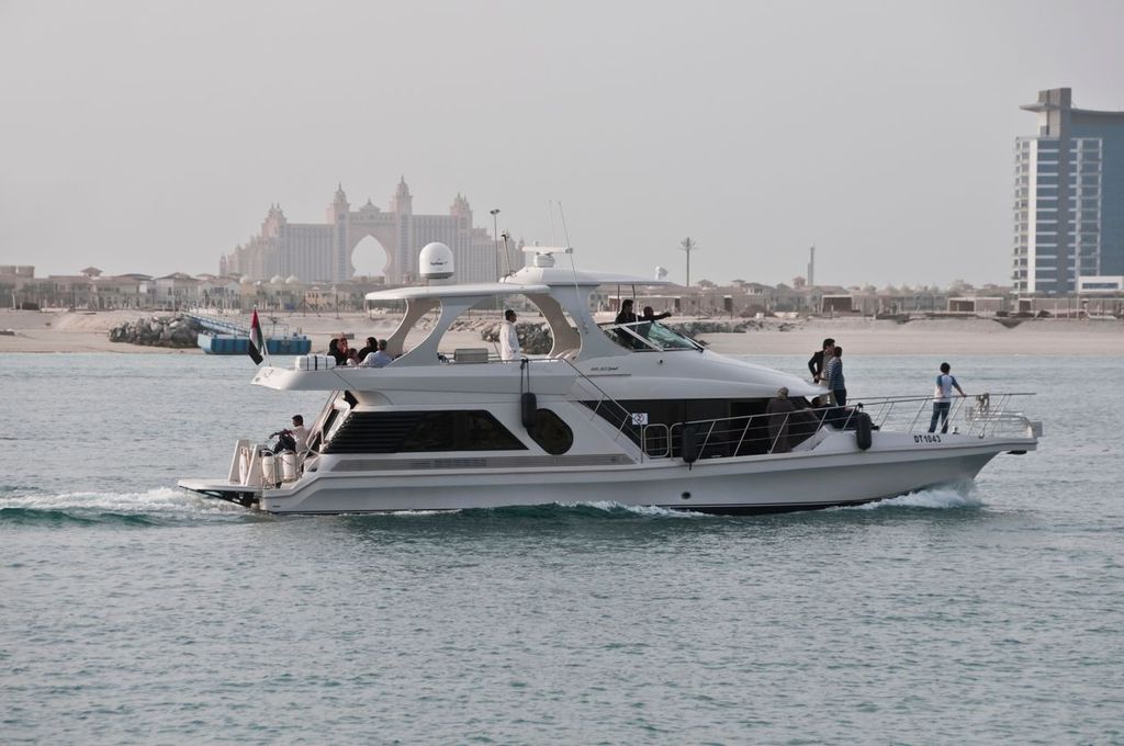 Families and tourists cruising on Luxury yacht in Dubai Marina with Atlantis Palm Jumeirah hotel at the background.