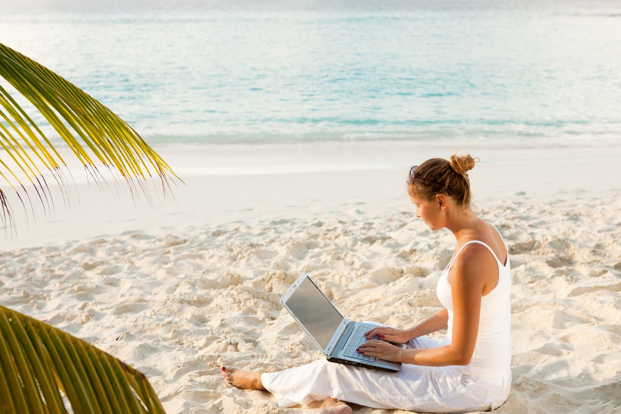 Woman booking vacation on her computer from the beach.