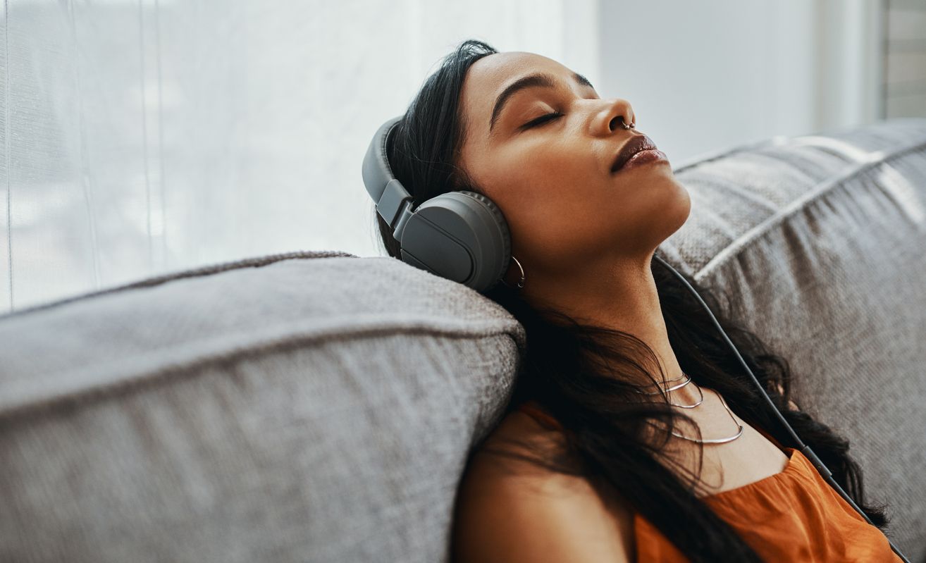 A young woman using headphones while relaxing on the sofa