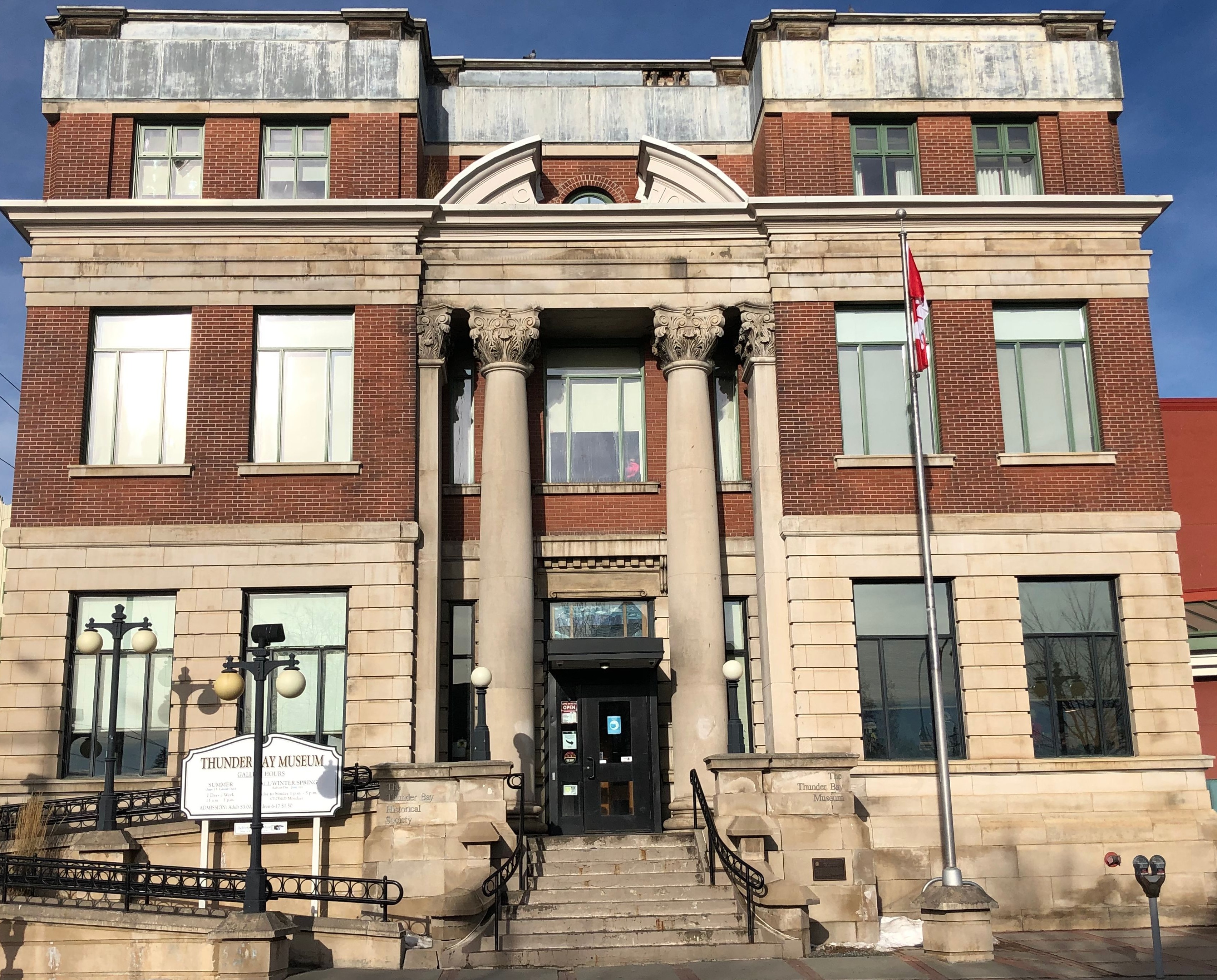 Thunder Bay Museum view from the front with sign in bottom left and Canadian flag on the right.