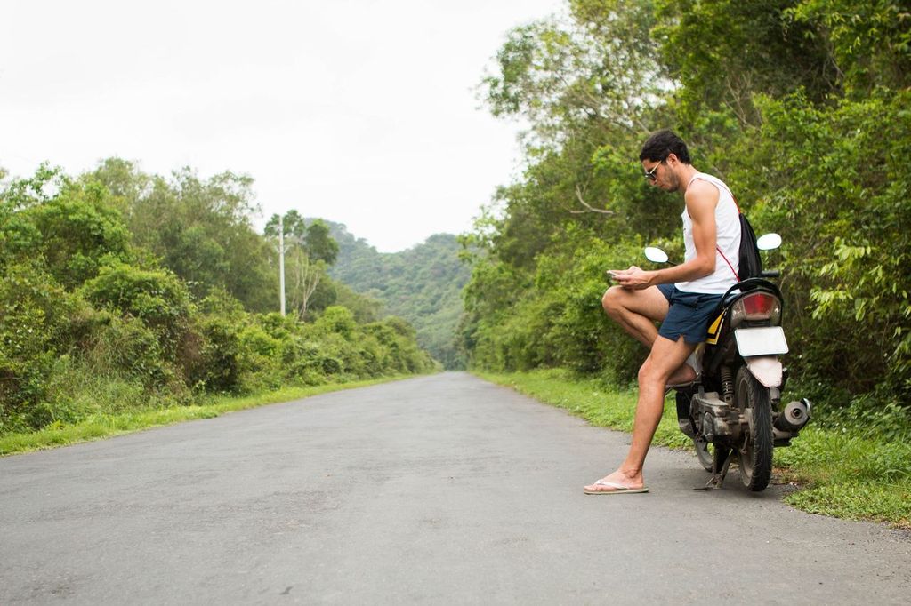 Young tourist rider sitting on a motorbike rental using a smartphone