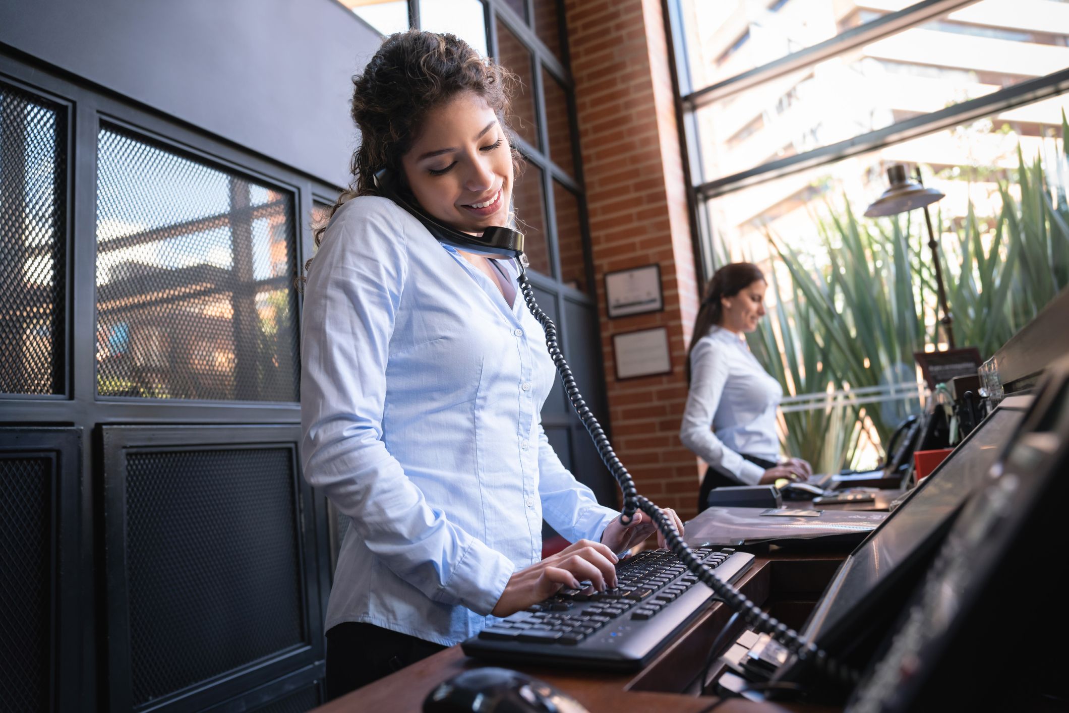 Hotel receptionist on a phone call looking at the bookings on system smiling