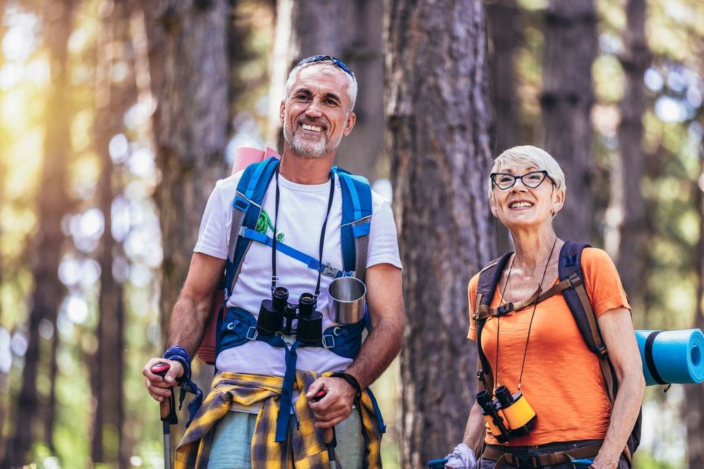 Senior couple hiking in forest wearing backpacks and hiking poles