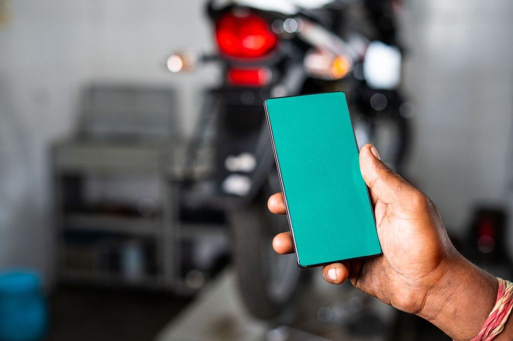Person showing green screen mobile phone at garage with bike in the background