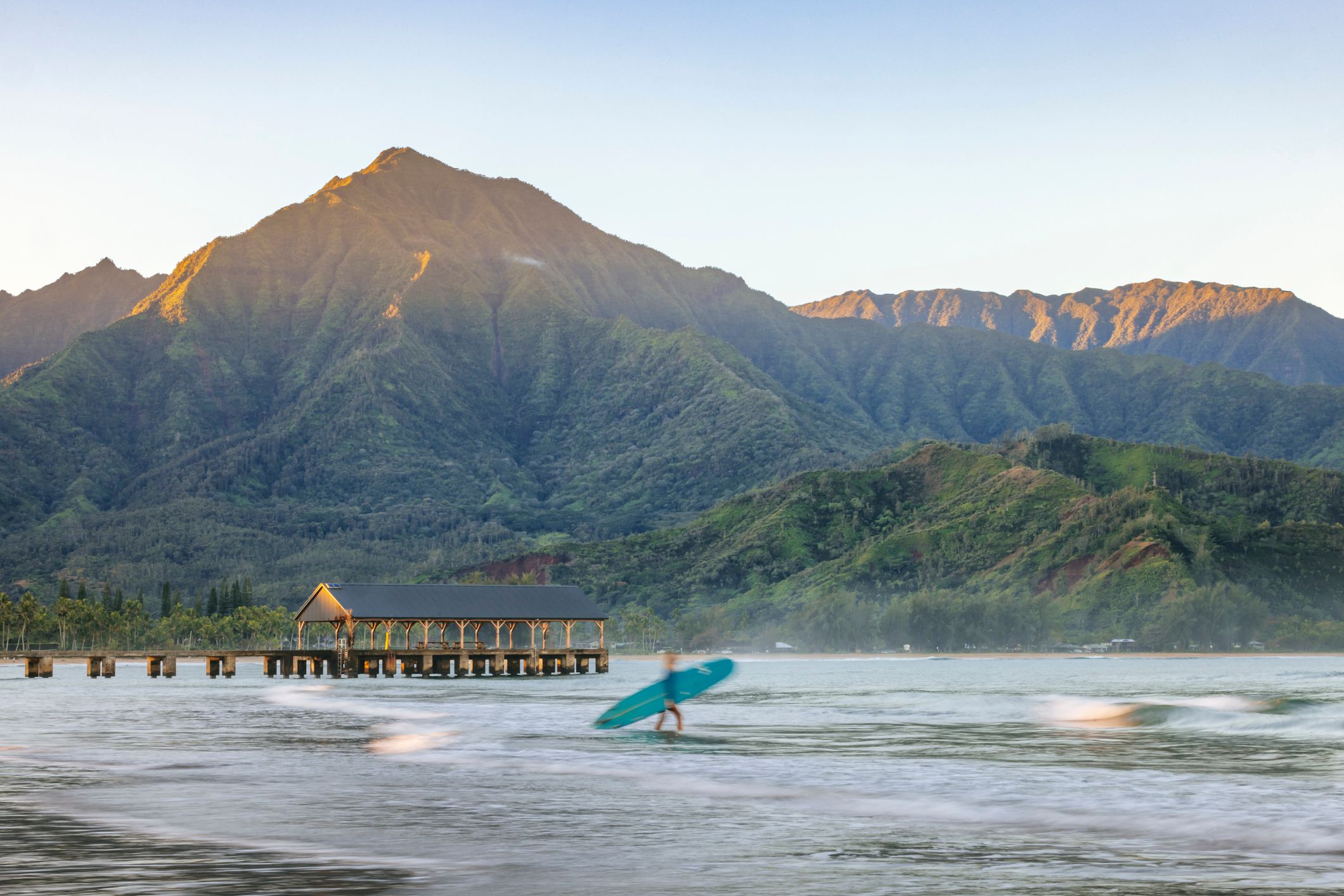 A woman is heading out for a surf in front of the pier at Hanalei Bay on the island of Kauai, Hawaii