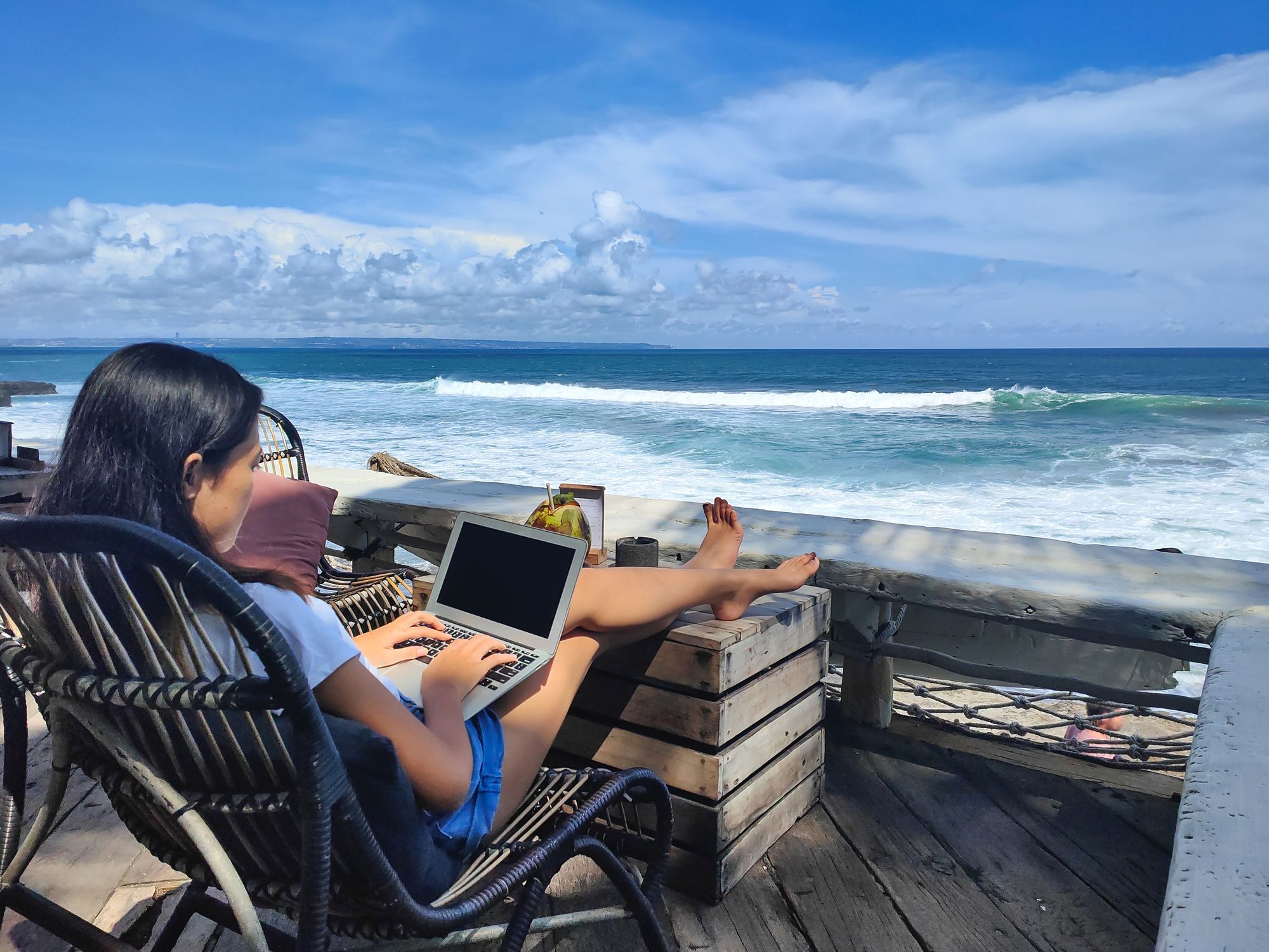 Young Indonesian woman working on a laptop with a beach view